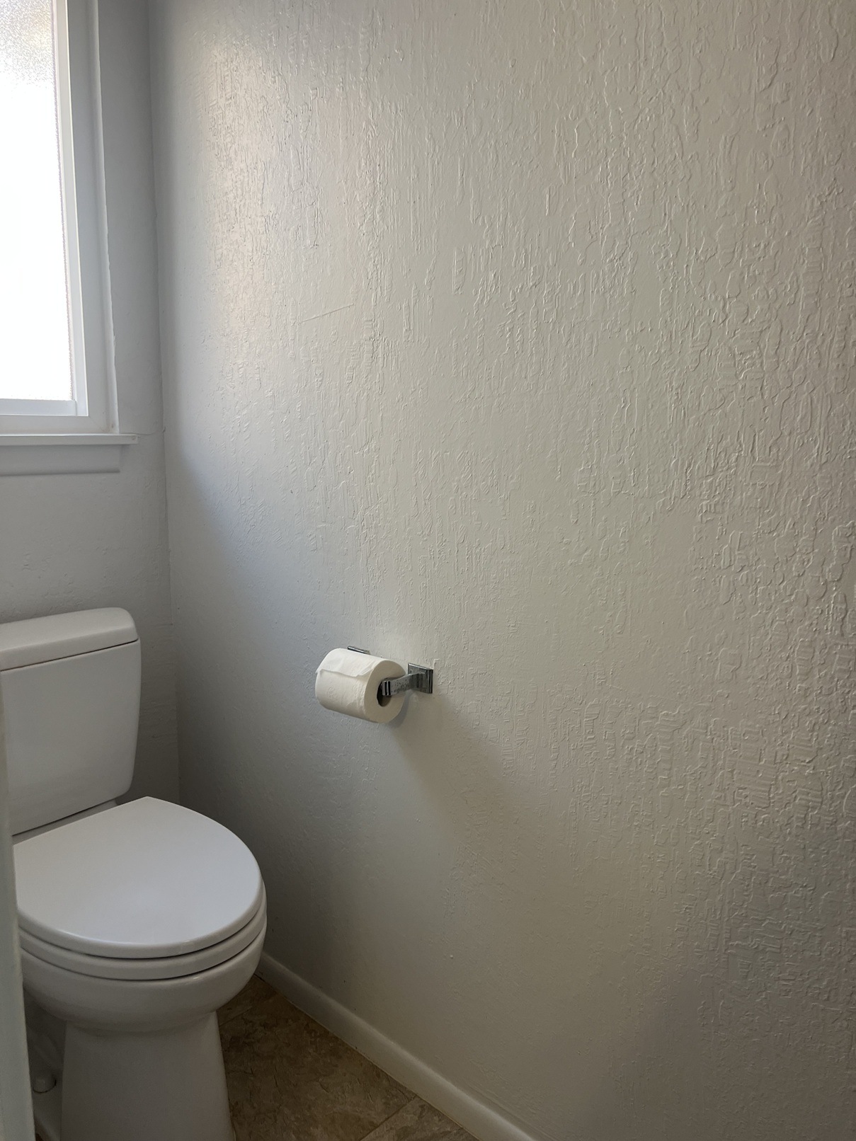 A white toilet in a bathroom with a white wall and a roll of toilet paper on the wall.